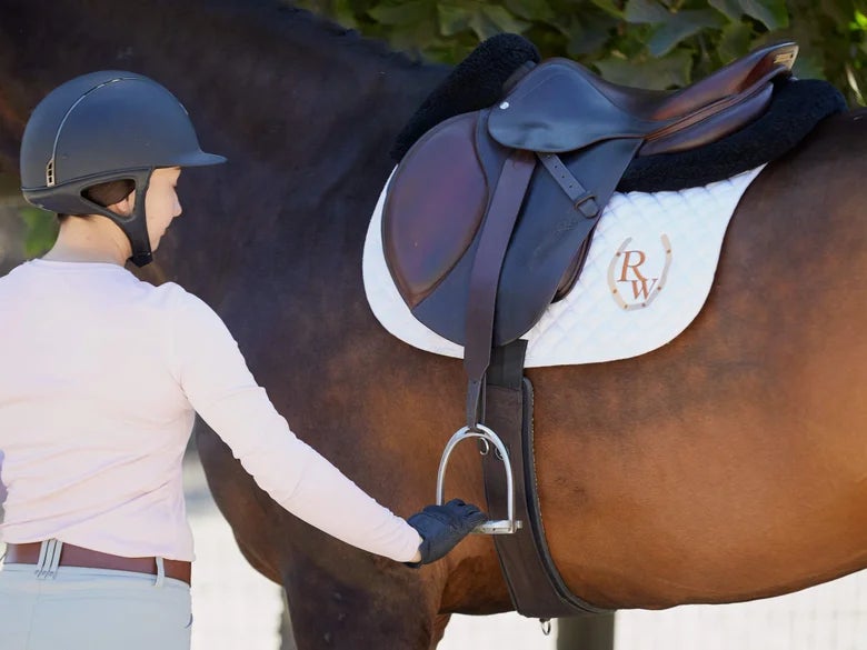 Rider pulling down stirrup leather on a tacked up bay horse.