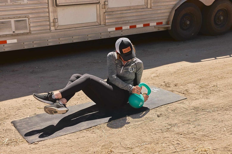 Woman demonstrating the Russian twist exercise with a kettlebell.