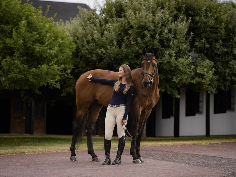 Girl wearing a TKEQ Equestrian Sun Shirt in black, standing next to her bridled bay horse.