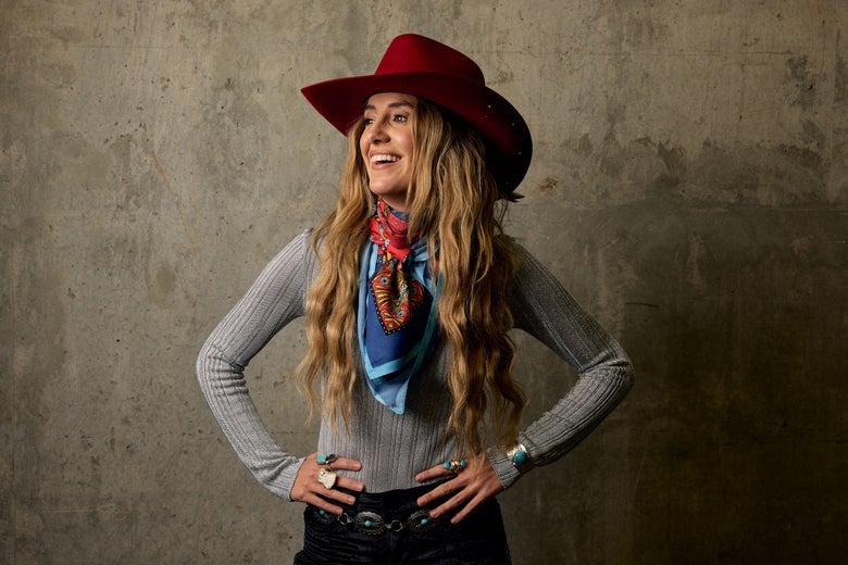 Smiling lady wearing a colorful wild rag and a red cowboy hat.
