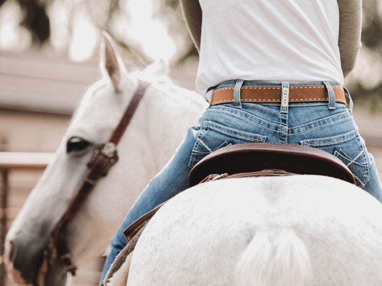 Women sitting on her white horse wearing mid-rise riding jeans