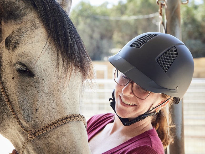 Women standing with her horse, wearing the TuffRider Starter riding helmet with carbon fiber.