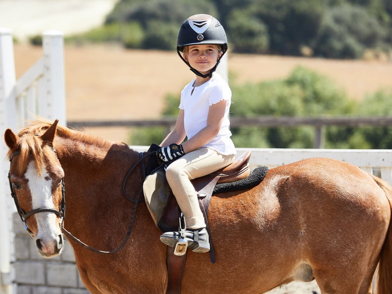 Little girl wearing a helmet and riding her chestnut pony