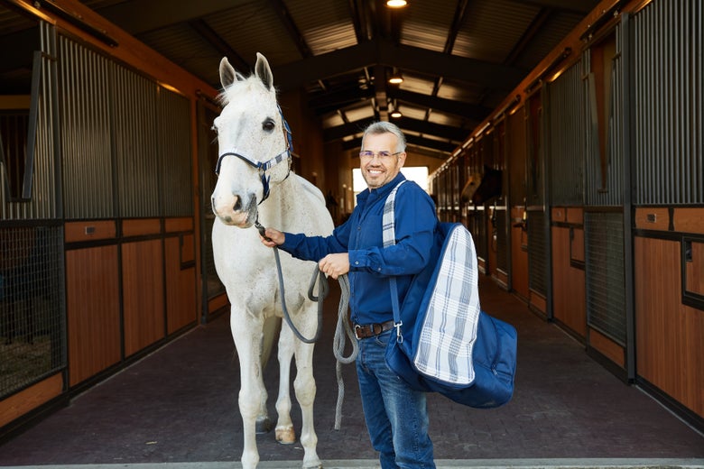 Man and horse standing in a barn wearing a Kensington halter and gear bag.