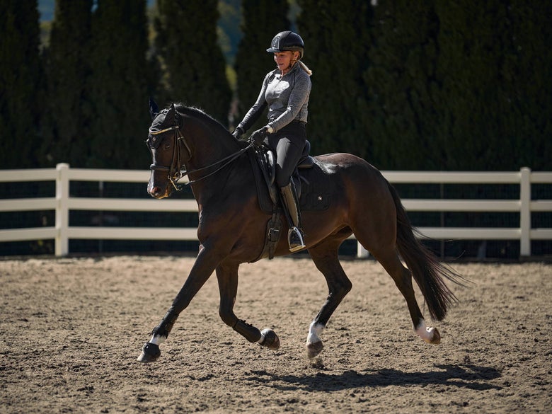 A woman riding a dark bay horse in a dressage arena.