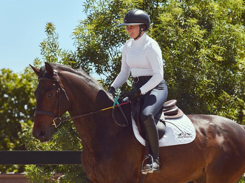 A rider riding her horse with rainbow reins.