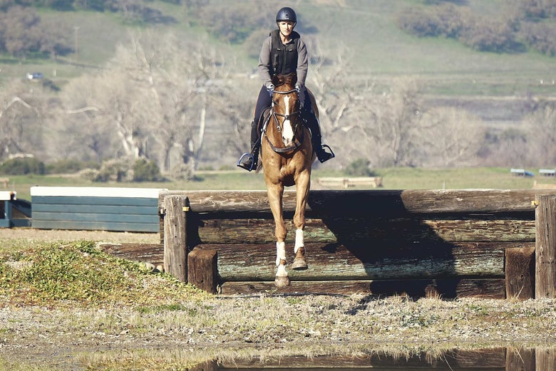 Bec Braitling riding a chestnut horse jumping a down bank on a cross country course.