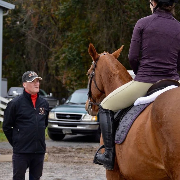Stephen Bradley talking with a student on horseback that's standing with her chestnut horse.