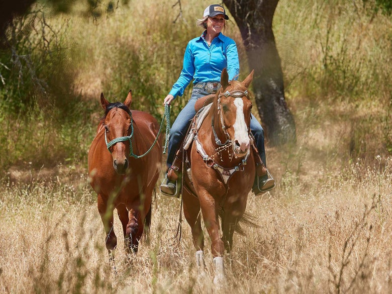 Krista riding down the trail, ponying another one of her horses.