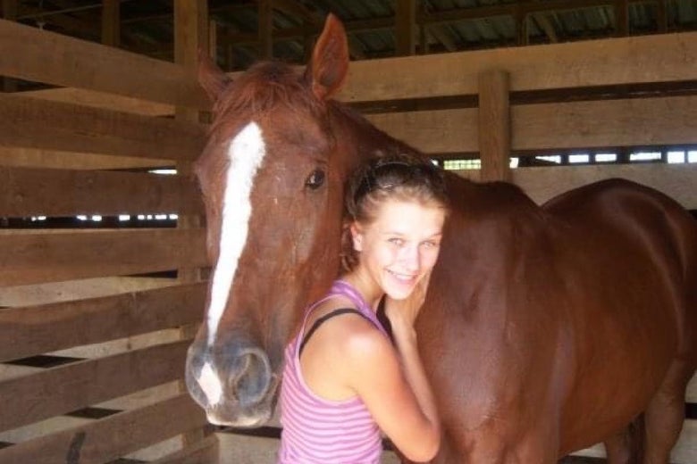 Liz Siadous in a purple and pink striped tank top standing next to her first horse, Dakota.