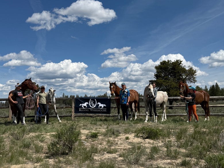Stevie Delahunt and a group of riders with their horses in front of a Riding Warehouse banner.