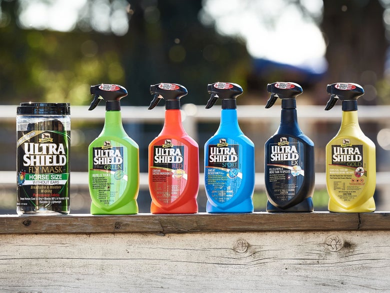 An assortment of Ultra Shield fly sprays and a fly mask by Absorbine for horses, all aligned on top of a fence