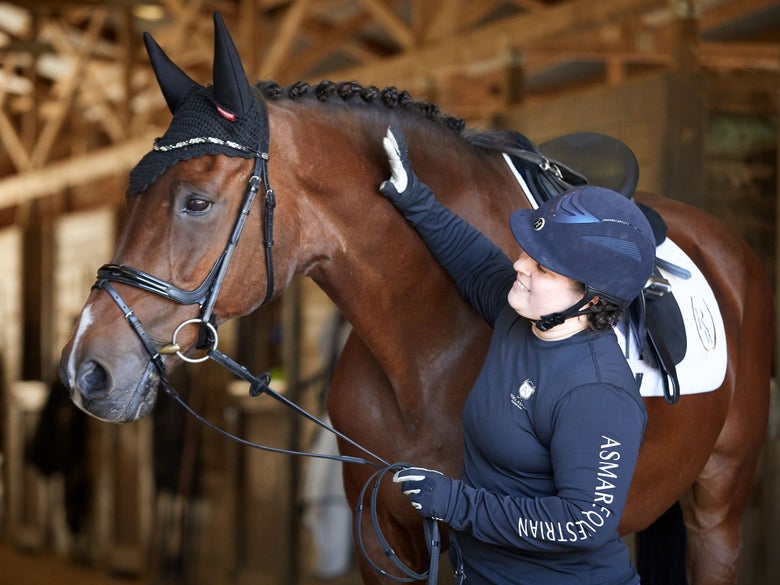 Dressage rider standing next to tacked up bay horse, petting its neck. 