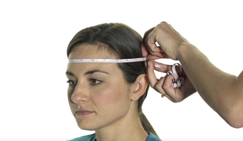 Soft tape measure being wrapped around widest part of woman's head for the circumference. 