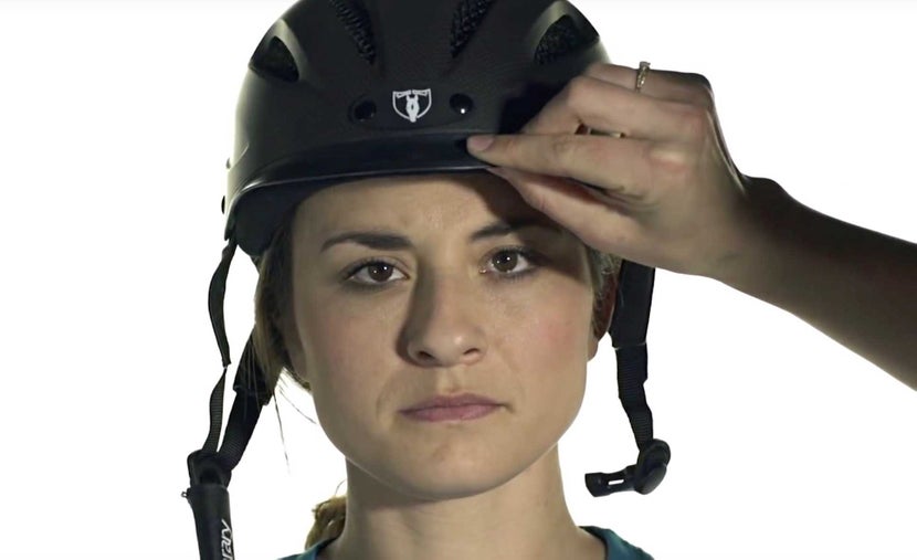 Tilting helmet on woman's head to check for proper fit. 