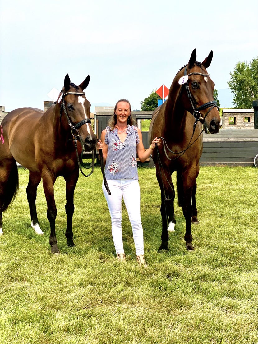 Andrea standing in grass holding Indy 500 and Junior by the reins. 