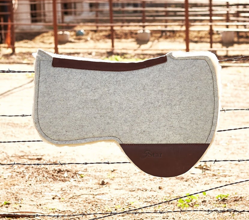 Barrel western saddle pad sitting on a barb wire fence.