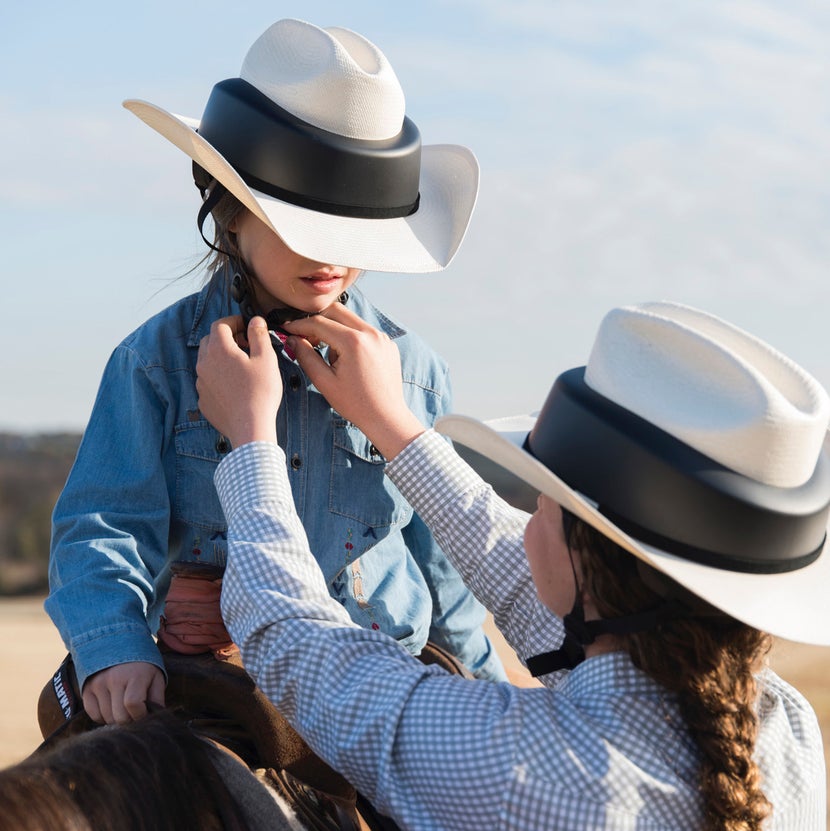 Women adjusting the harness of a Resistol Ridesafe Cowboy Hat Helmet on a child