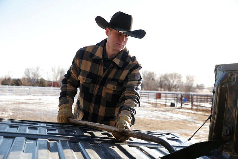 Man in winter attire loading shovel into truck. 