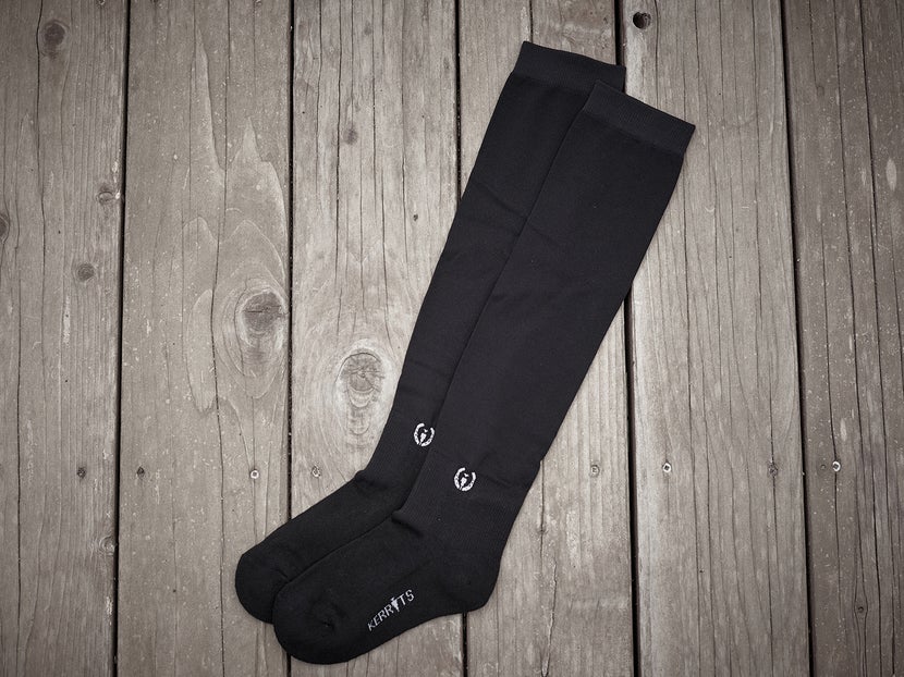 A black pair of the Kerrits Dual Zone Socks laying flat against a wooden blackground. 