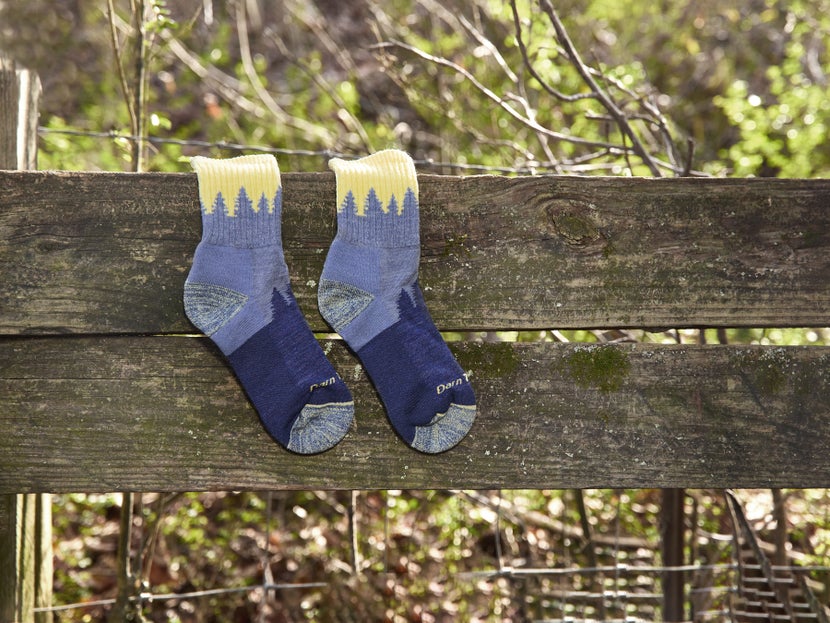 The Darn Tough Treeline Merino Wool Crew Socks in Light Denim laying flat against a wooden fence. 