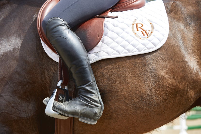 A woman wears the Freejump Soft'Up Classic Single Branch Stirrups while riding a horse. 