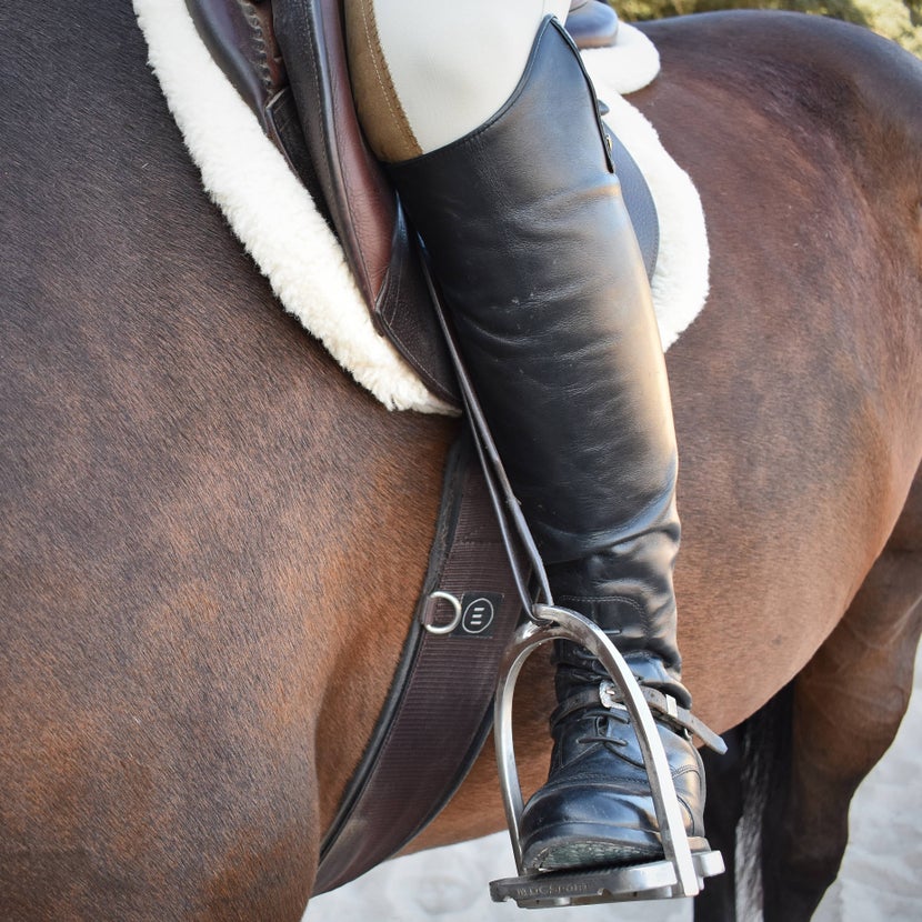 A woman wears the MDC 'S' Classic Aluminum Stirrups while riding a horse. 