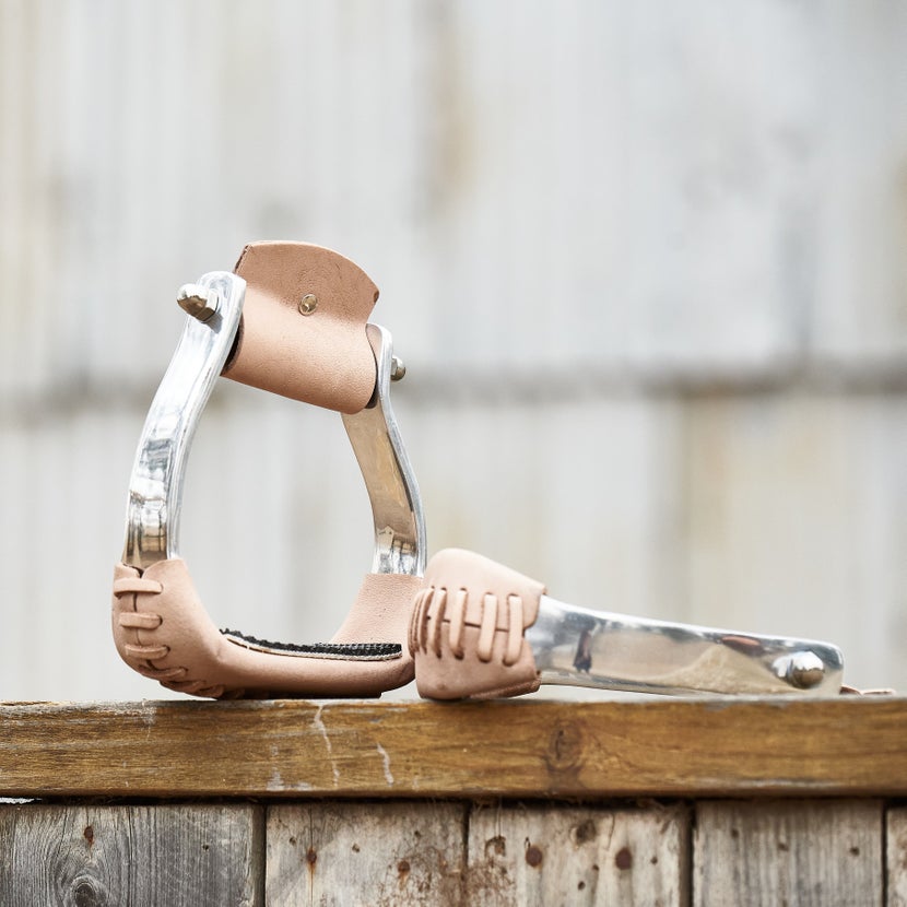 The Tough 1 Lightweight Aluminum Angled Western Stirrups sitting on a weathered, wooden fence. 