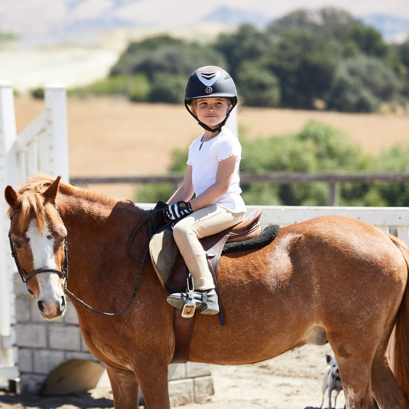 A little girl wears Centaur Fillis Peacock Stirrups while riding a horse. 