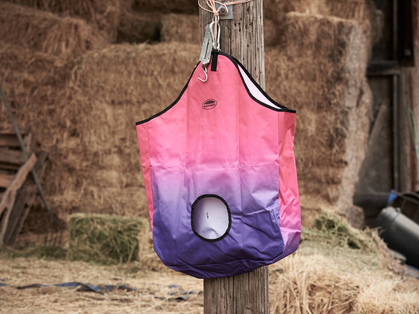 Weatherbeeta Ombre Hay Bag hanging on pole with hay in the background. 