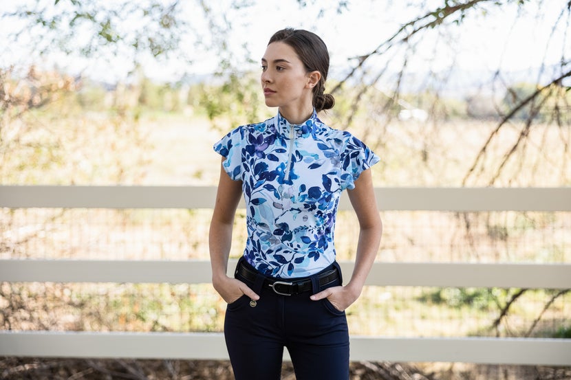 Woman wearing a Kastel Ruffle Short Sleeve Sun Shirt, standing next to a white fence. 
