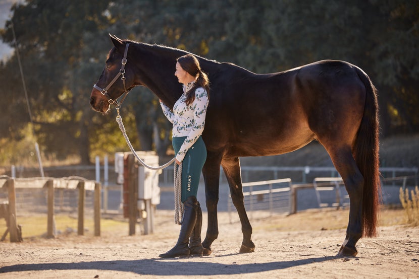 Woman riding her horse wearing Kerrits Sit Tight Wind Pro Full Seat Tights and Kerrits Muzzle Nuzzle Fleece Half Zip Top.