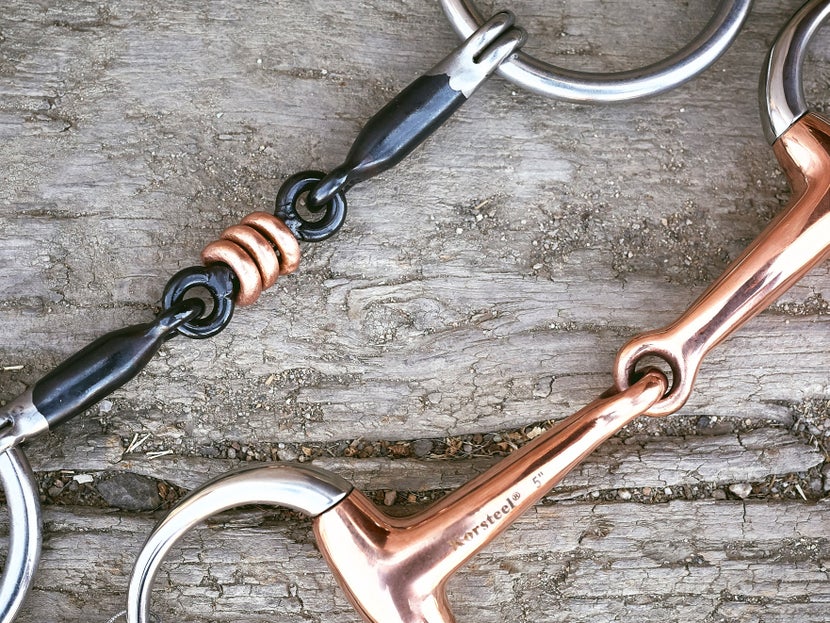 Close up image of a copper bit and sweet iron bit laying side-by-side on a piece of wood.