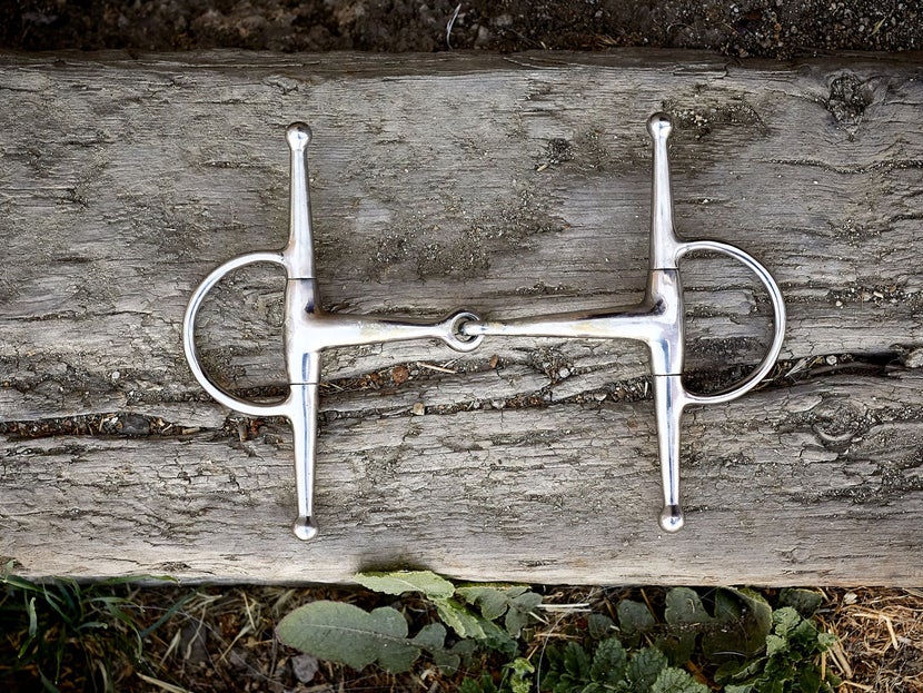 Image of a full-cheek horse bit sitting flat on a piece of wood. 