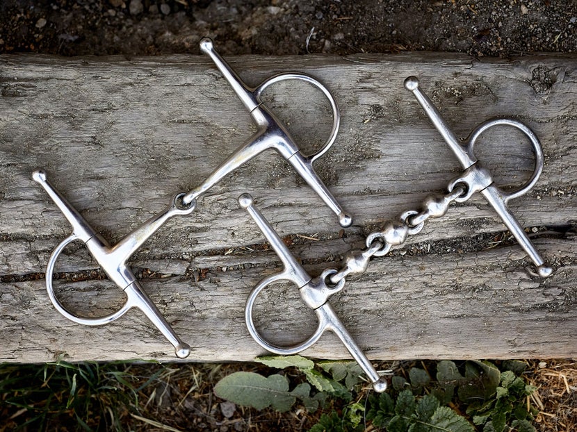 Two horse bits with full-cheek cheekpieces, laying side-by-side on a piece of wood. 