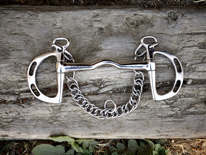 A horse bit with kimberwick cheekpieces, laying flat on a piece of wood. 