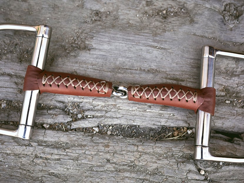 Close up image of a bit wrapped in leather, laying flat on a piece of wood. 