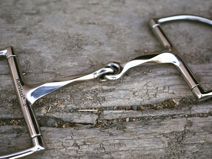Close up image of a stainless steel bit, laying flat on a piece of wood. 