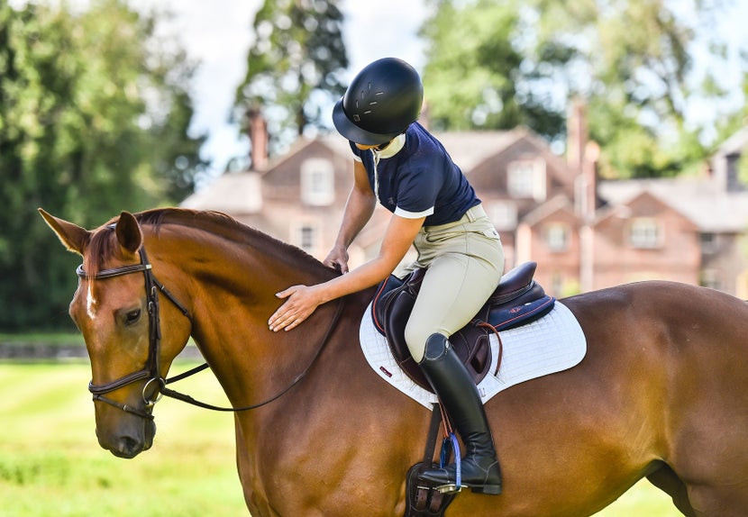 Women patting her horse, wearing a Charles Owen helmet. 