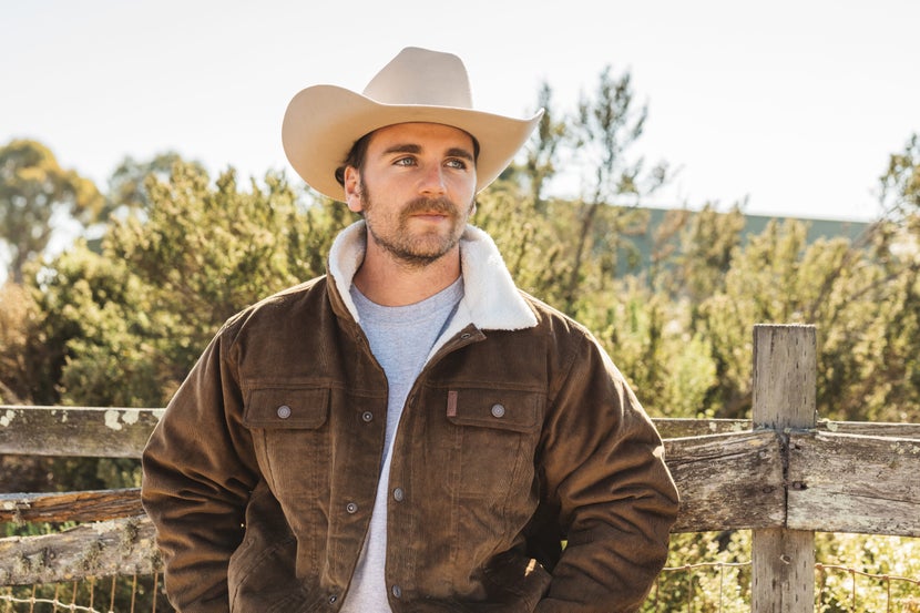 Man standing in front of wooden fence, wearing felt cowboy hat. 