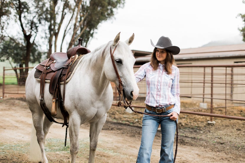 Woman standing with horse wearing grey cowboy hat. 