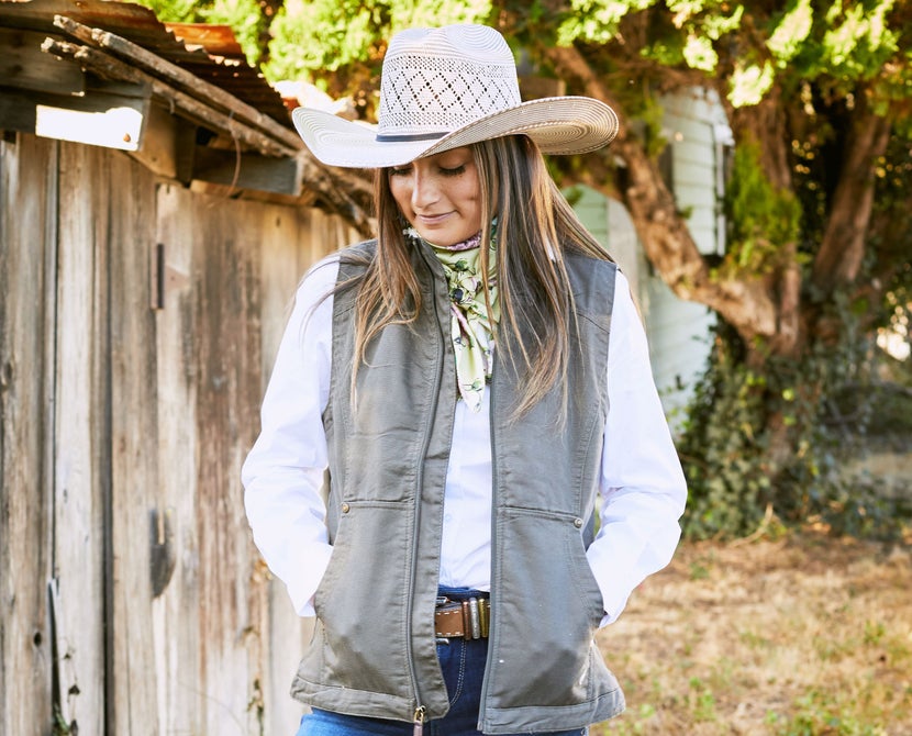 Woman standing in Western attire, wearing a straw cowboy hat. 