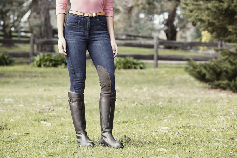 A horse rider stands in knee patch denim breeches. 