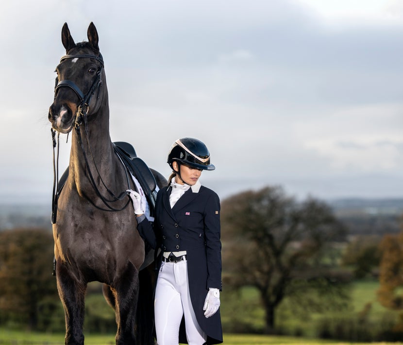 Rider in full dressage show attire standing next to her horse, also dressed in full dressage tack. 