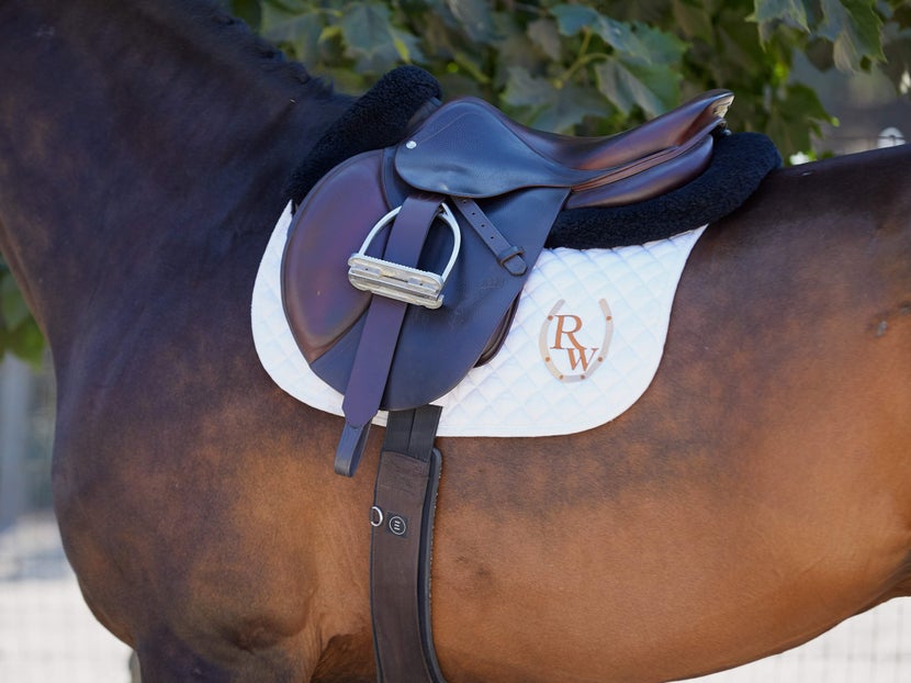 a saddled horse with a half pad on top of a square English pad