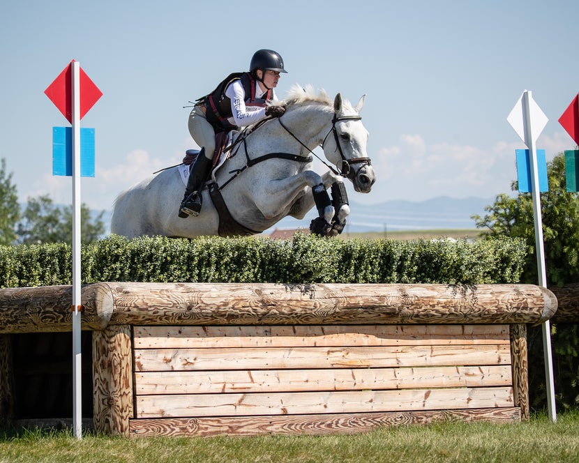 Women wearing the Hit Air Safety Vest while jumping a white horse over a brush cross country fence.