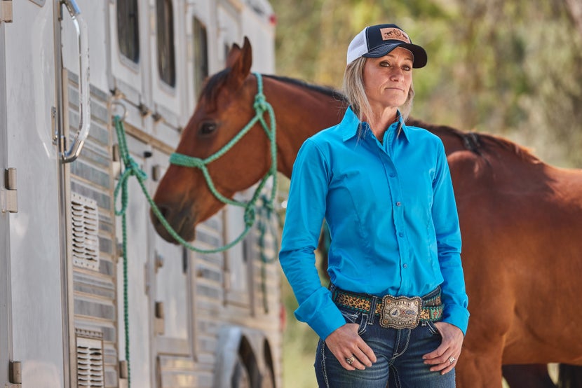 Krista standing next to her bay horse tied at the horse trailer. 