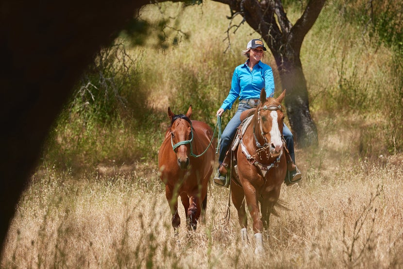 Krista riding one horse (chestnut) and ponying the other (bay) while they get out of the arena. 