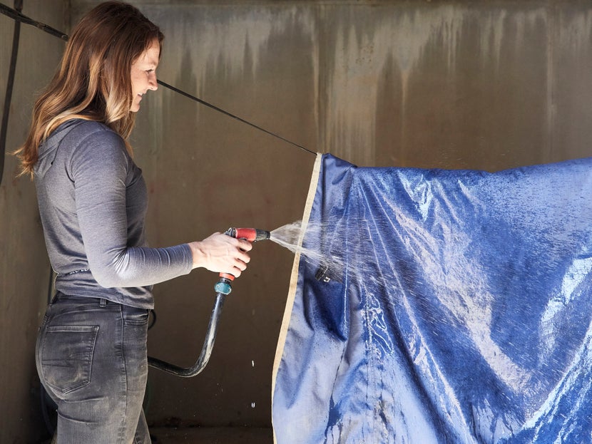 Girl washing a horse blanket with a hose.
