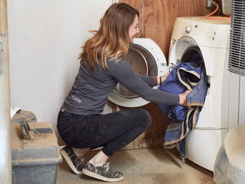 girl putting a horse blanket in a washer machine